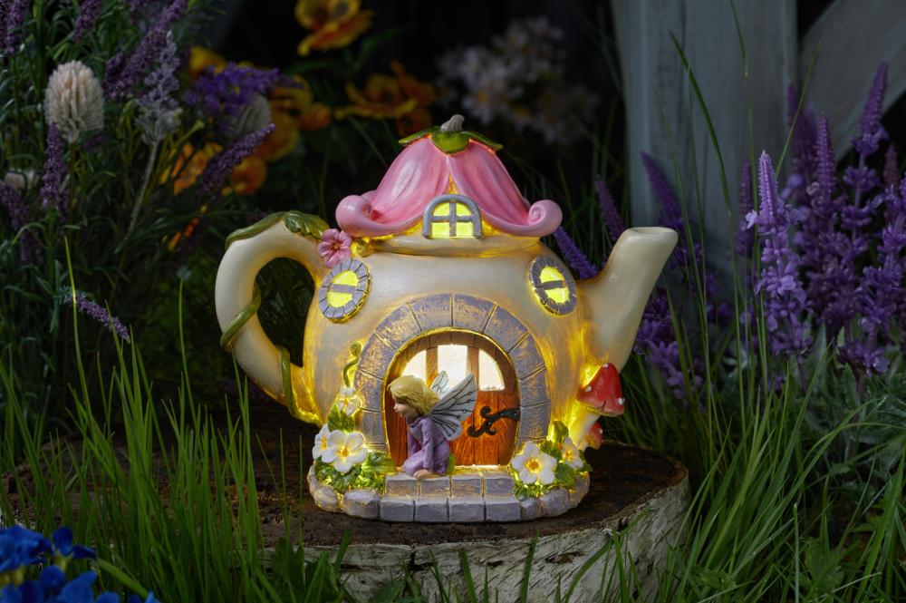 Feenhaus in Form einer Teekanne im Garten stehend, beleuchtet.